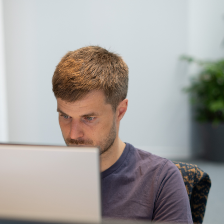 Close-up van een geconcentreerde UX specialist die aandachtig naar een scherm kijkt in een lichte kantooromgeving met planten op de achtergrond