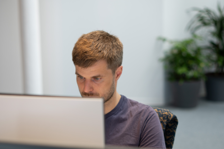 Close-up van een geconcentreerde UX specialist die aandachtig naar een scherm kijkt in een lichte kantooromgeving met planten op de achtergrond